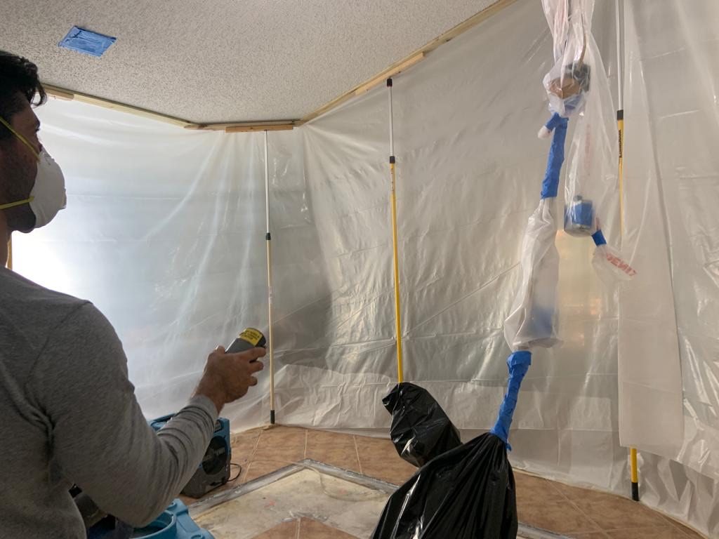 Disaster Recovery Experts technician in a respirator taking a moisture reading inside a sealed containment area